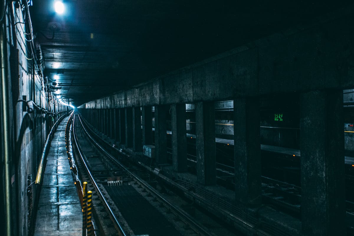 View down a dark underground railway tunnel with tracks stretching into the distance